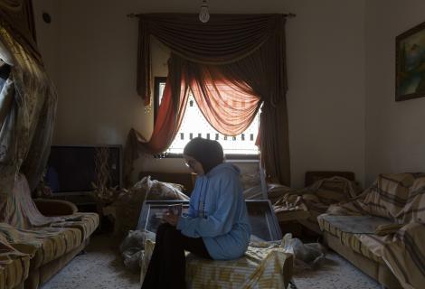 A young woman from Lebanon looks at a family photo album in her living room, which was damaged after it was bombed by Israeli forces. 